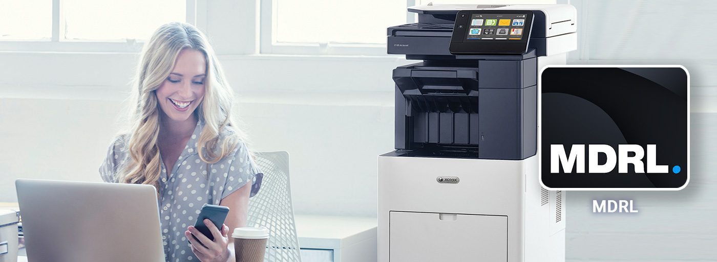 Femme souriante travaille devant ordinateur et téléphone portable à côté d'une imprimante Xerox