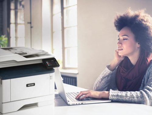 Jonge vrouw die op haar computer werkt naast een Xerox® B315 multifunctionele printer.
