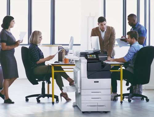Team aan het werk in een kantoor met bedrukte papieren en de multifunctionele kleurenprinter Xerox® VersaLink® C7100 serie